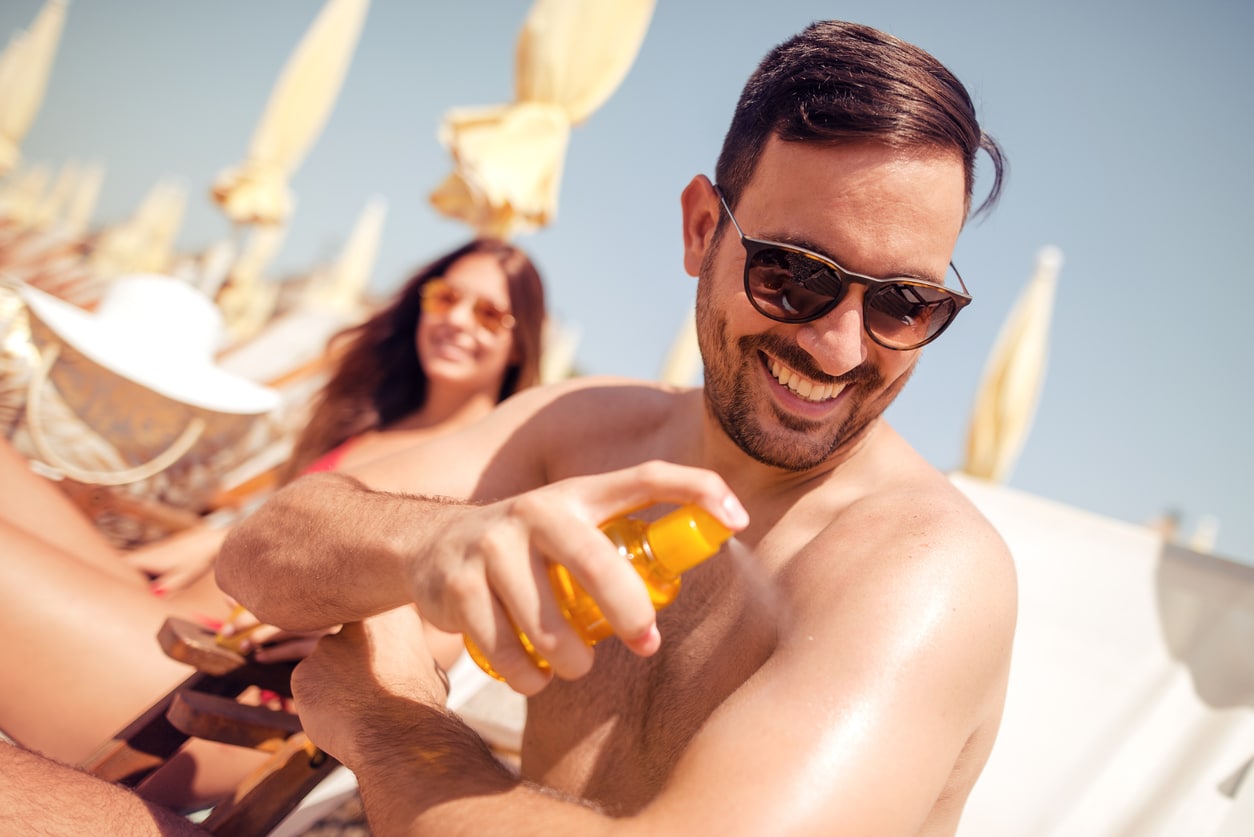 Happy couple smiling on the beach, man applying sun cream.