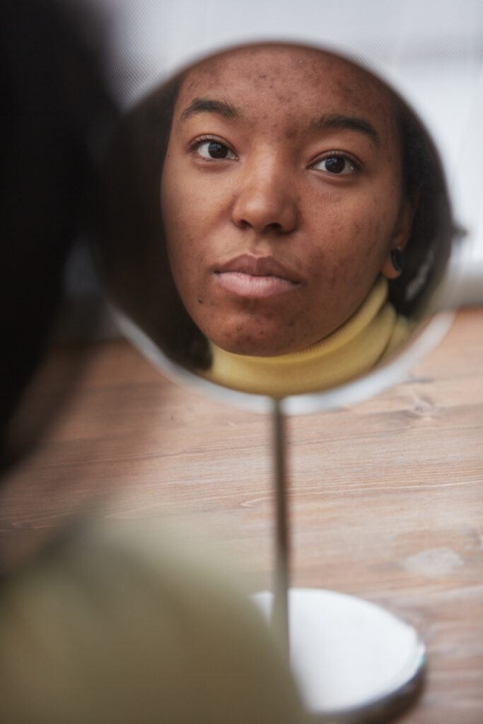 Reflection of African American woman looking in mirror with focus on skin imperfections