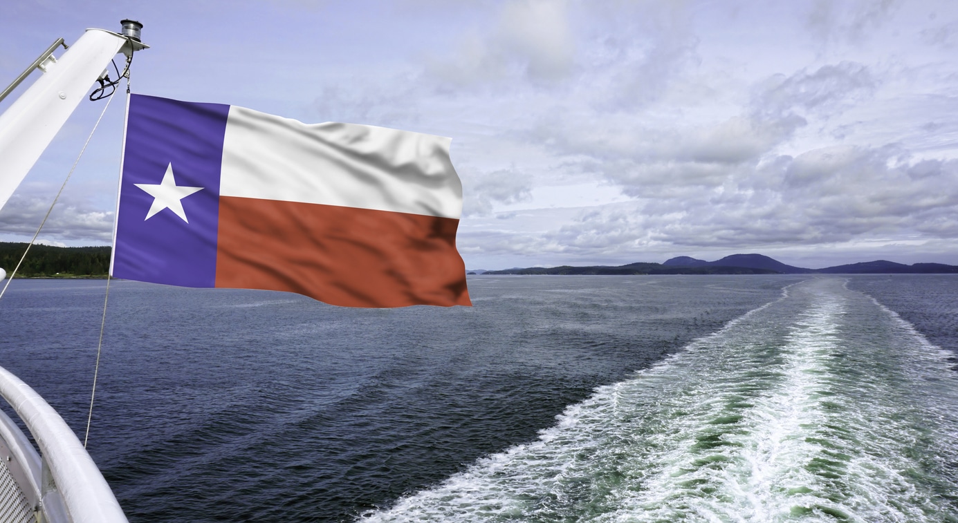 Texas flag flying high against the blue water waves.